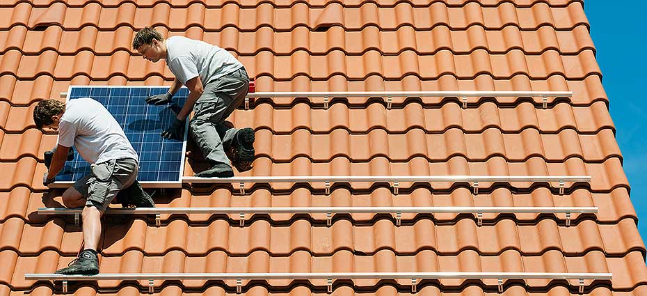 Twee mannen plaatsen zonnepanelen op een schuin dak.